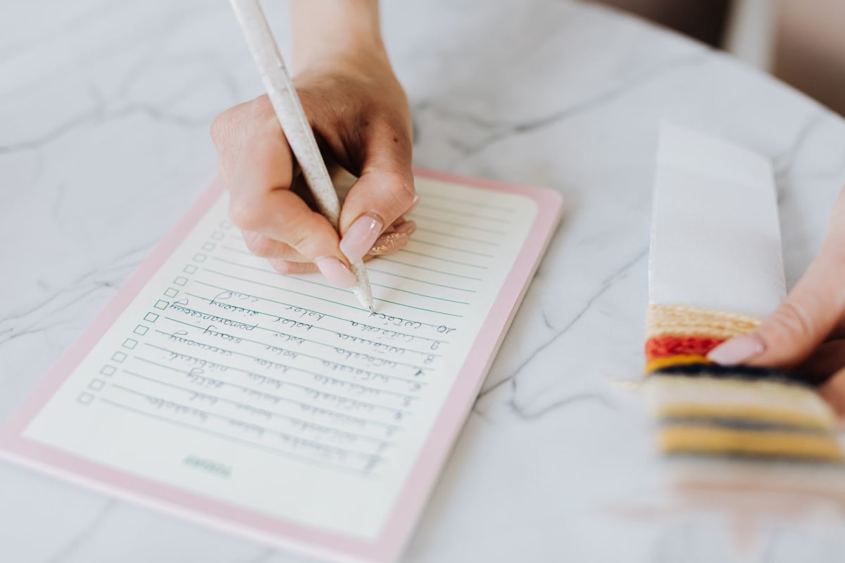 hand writing checklist on lined paper notebook with pen, close-up workspace